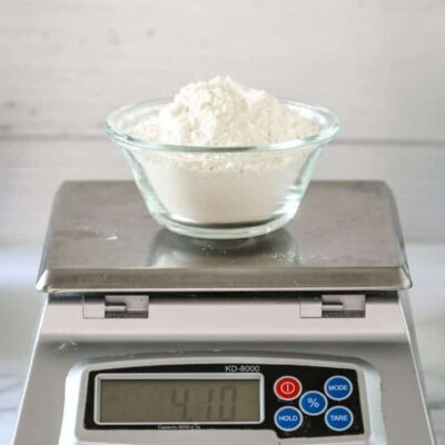 A cup of flour on a scale, making cake flour with all-purpose and cornstarch.