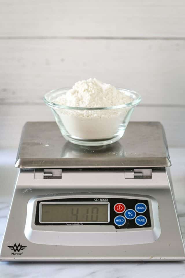 A cup of flour on a scale, making cake flour with all-purpose and cornstarch.