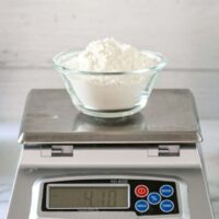 A cup of flour on a scale, making cake flour with all-purpose and cornstarch.