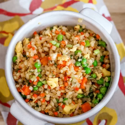 Fried rice with mixed vegetables in a white mug on a colorful cloth.