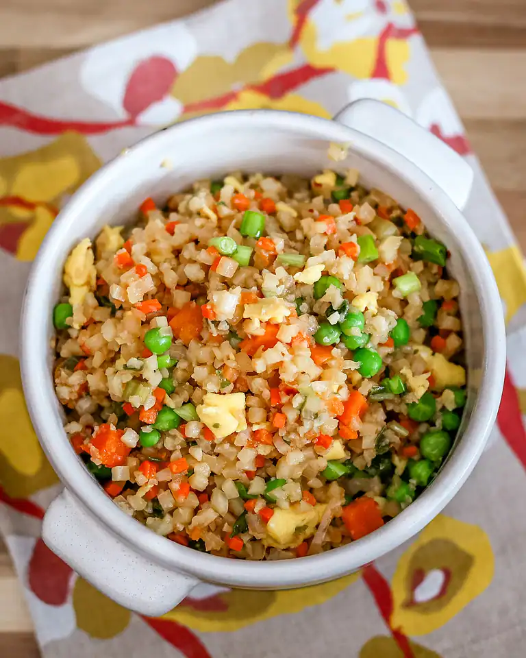 Fried rice with mixed vegetables in a white mug on a colorful cloth.
