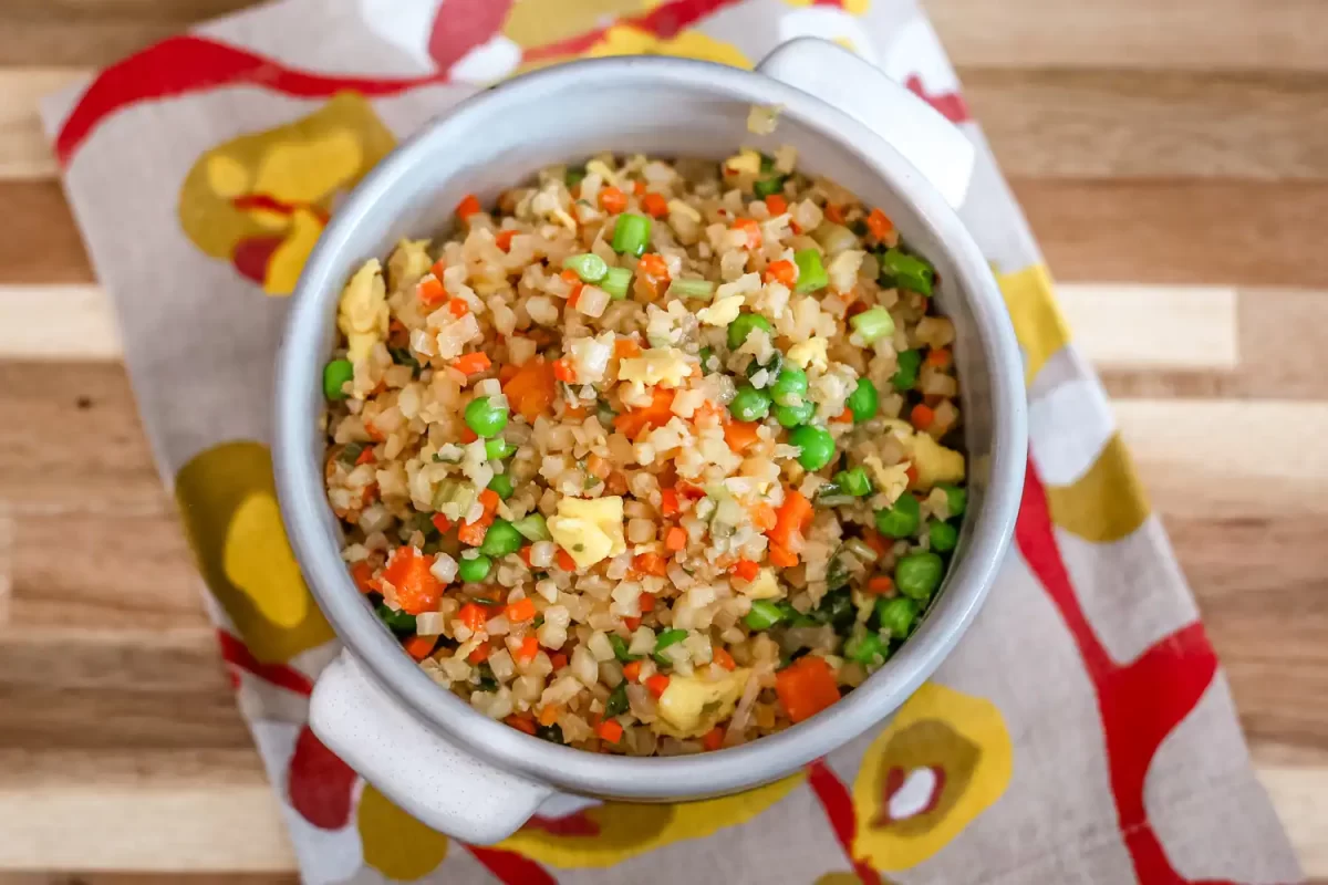 Steamed cauliflower rice with mixed vegetables in a white bowl on a wooden table.