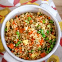 Closeup of cauliflower fried rice in a bowl, showing the fluffy eggs, peas, and carrots.