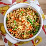 Cooked vegetable fried rice with peas, carrots, and scrambled eggs in a white cup.