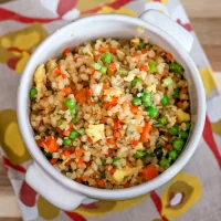 Cooked vegetable fried rice with peas, carrots, and scrambled eggs in a white cup.