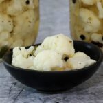 cauliflower pickles in a small bowl with jars in the background.