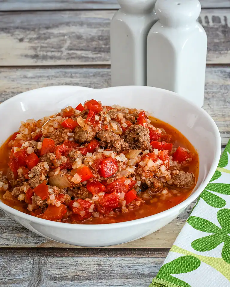 Rich beef and vegetable stew in a white bowl on a rustic wooden table.