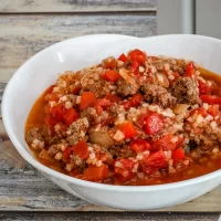Ground beef and vegetable stew in a white bowl on a wooden surface.