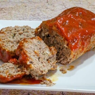 A tasty loaf of cheddar and tomato soup meatloaf on a platter, sliced.