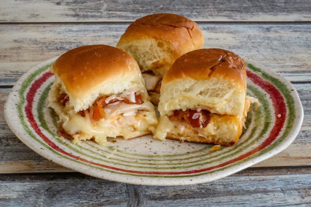 Three baked chicken, bacon, and cheese sliders with sriracha mayo on a plate
