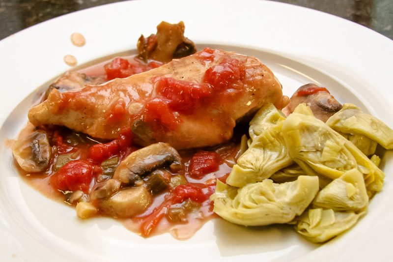 chicken breast with tomato and mushroom sauce on a plate with artichokes on the side