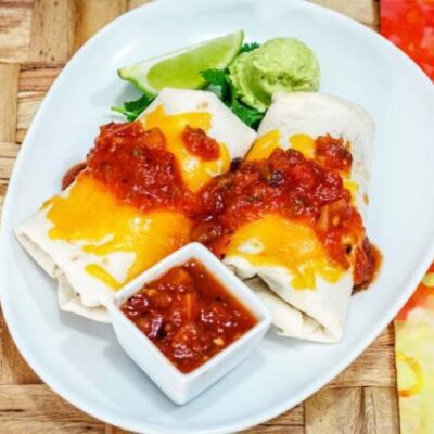 chicken burritos on a plate with salsa and guac