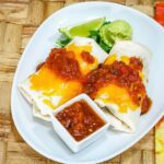 chicken burritos on a plate with salsa, guacamole, and limes