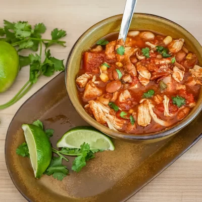 Savory chicken and bean chili in a rustic bowl with lime and cilantro garnishes.