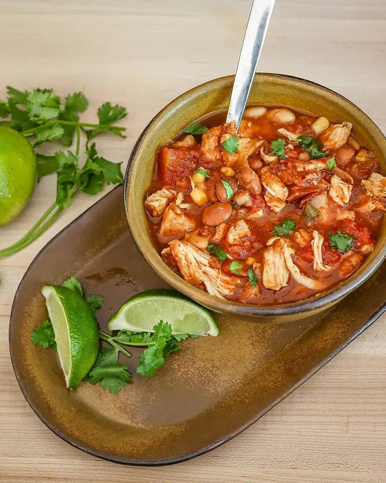 Savory chicken and bean chili in a rustic bowl with lime and cilantro garnishes.