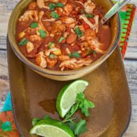 A big bowl of chicken chili stew with lime wedges and cilantro.