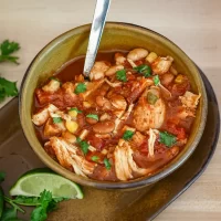 Savory chicken and bean soup with cilantro and lime wedges.