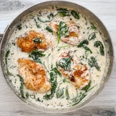 Baked chicken breasts simmering in a creamy spinach sauce.