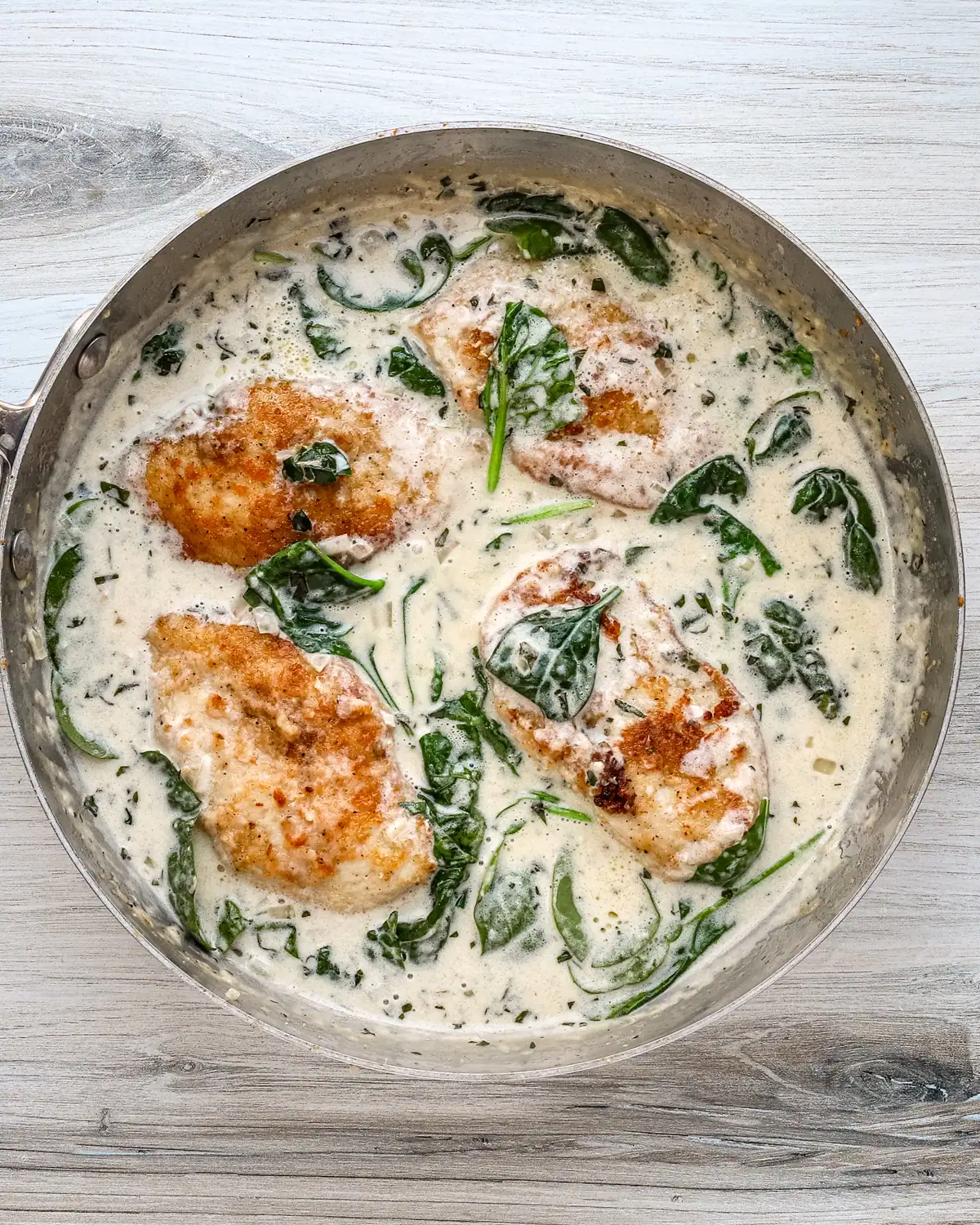 Baked chicken breasts simmering in a creamy spinach sauce.