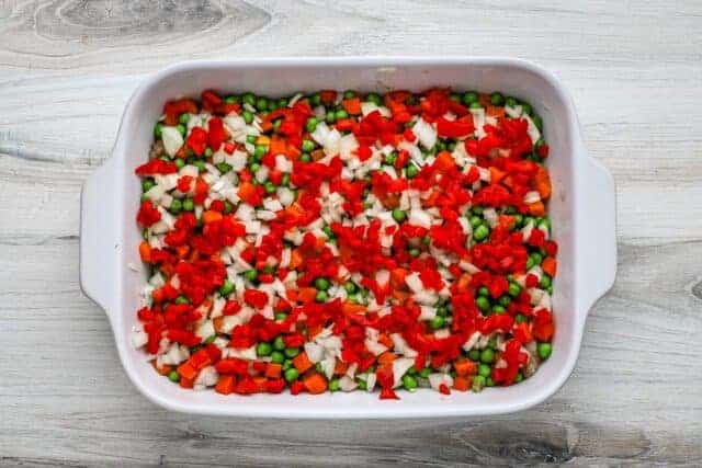 Chicken pot pie casserole prep: Layers of peas and carrots, onions, and pimientos.