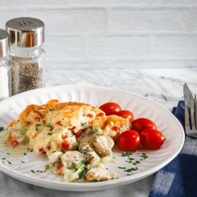 A plate with a helping of chicken pot pie casserole with a garnish of parsley and some grape tomatoes on the side.