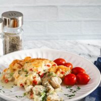 A plate with a helping of chicken pot pie casserole with a garnish of parsley and some grape tomatoes on the side.