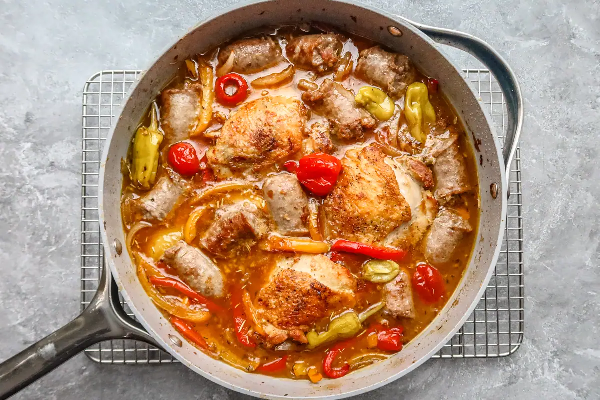 Chicken scarpariello with chicken thighs and sausage and peppers in a skillet.