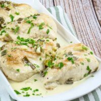 Chicken breasts on a serving platter with creamy champagne sauce and parsley garnish.