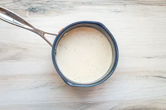 A saucepan with white wine cream sauce for chicken breasts with Gruyère and spinach.