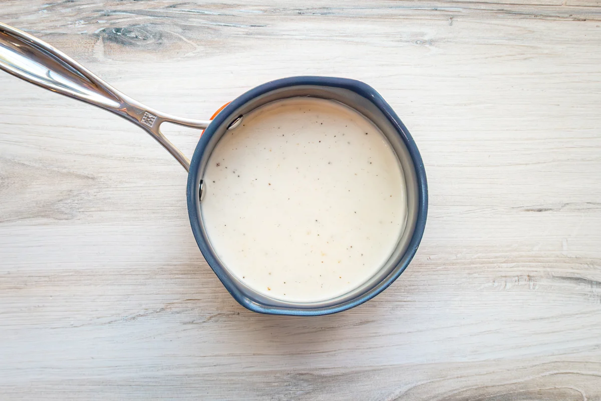 A saucepan with white wine cream sauce for chicken breasts with Gruyère and spinach.