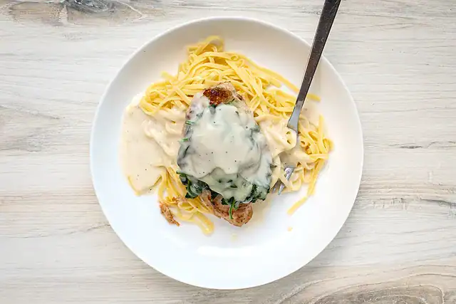 Chicken breasts topped with wilted spinach and shredded Gruyère cheese, on pasta with white wine sauce.