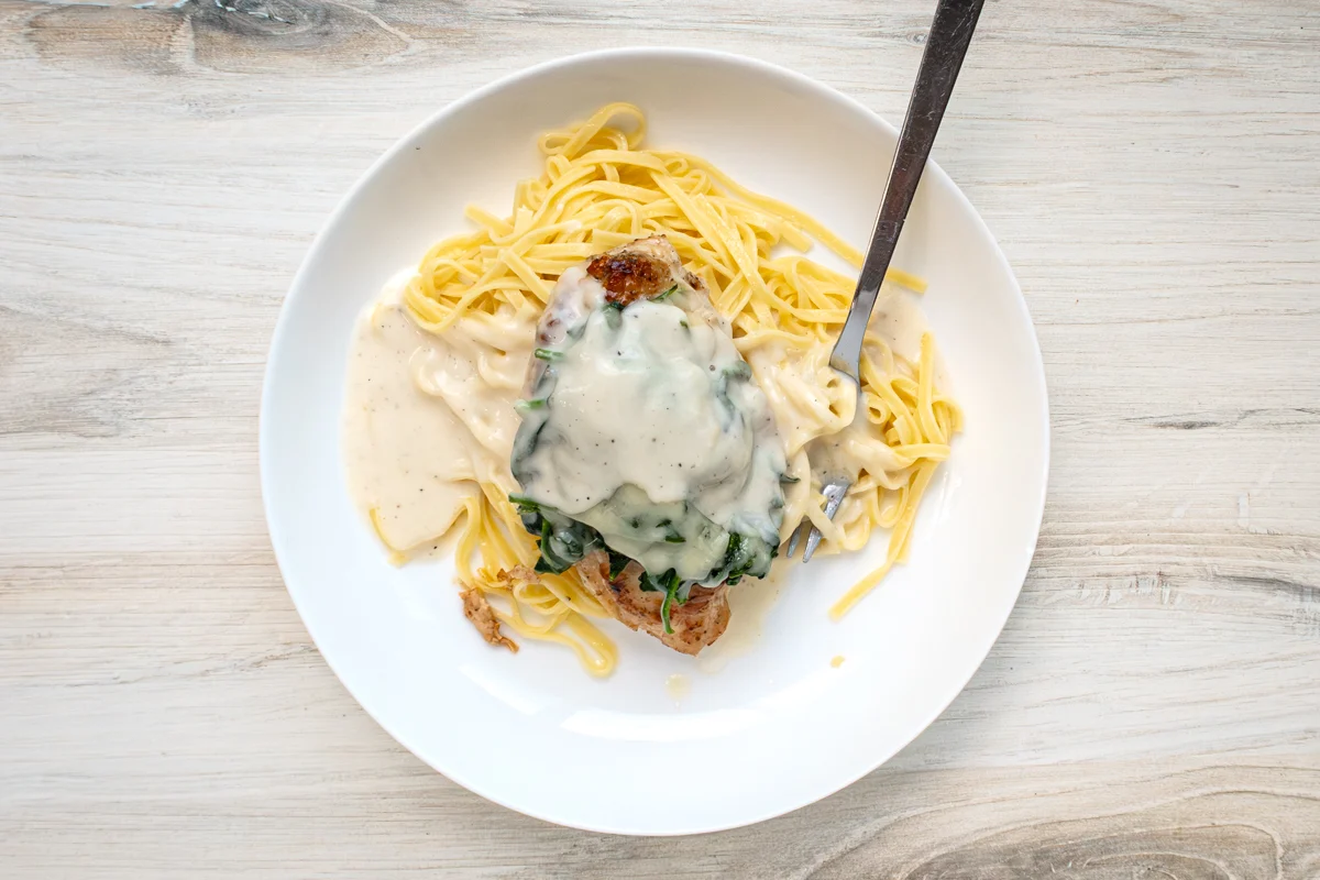 Chicken breasts topped with wilted spinach and shredded Gruyère cheese, on pasta with white wine sauce.
