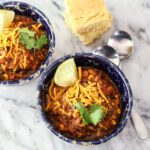 chili in bowls with garnishes and cornbread