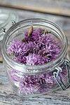 Preserved purple chive blossoms in a glass jar on a wooden surface.