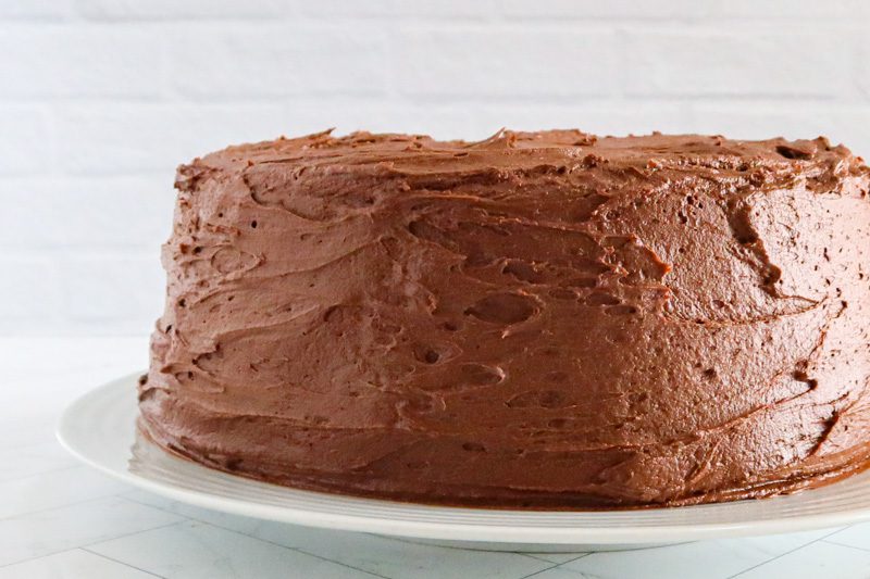 chocolate buttercream frosting on a layer cake on a white plate