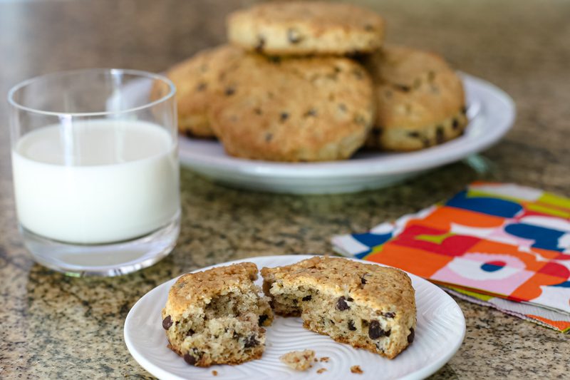 chocolate chip scone on a plate with more in the background and a glass of milk
