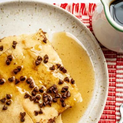 Slices of sheet pan pancakes on a plate with chocolate chip topping and syrup on the side.