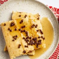 Slices of sheet pan pancakes on a plate with chocolate chip topping and syrup on the side.