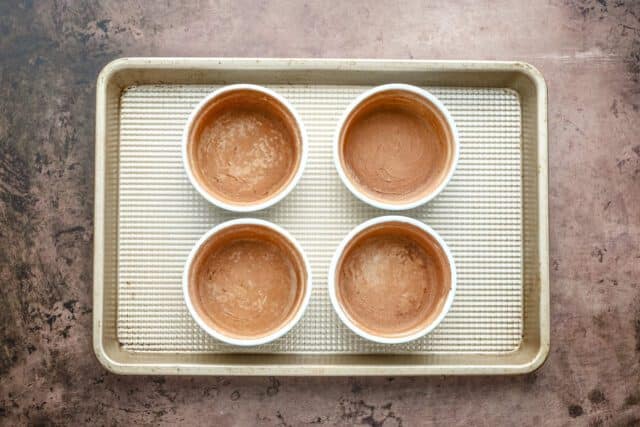 Small ramekins filled with melted chocolate on a baking tray.