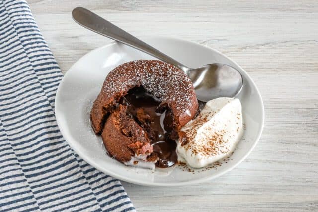 Rich molten chocolate fondant with melting center and whipped cream on side.