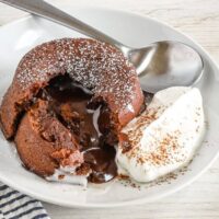 Rich molten chocolate lava cake with melting center and whipped cream on a white plate.