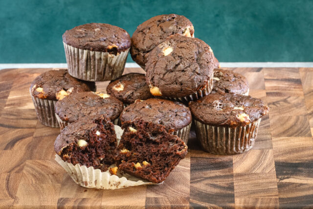 Chocolate zucchini muffins with white chocolate chips, baked, with one split to show the texture.