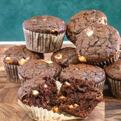 Chocolate zucchini muffins with white chocolate chips, baked, with one split to show the texture.