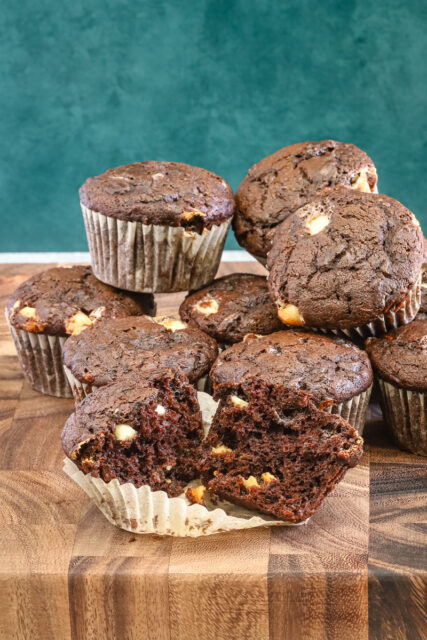 Chocolate zucchini muffins with white chocolate chips, baked, with one split to show the texture.