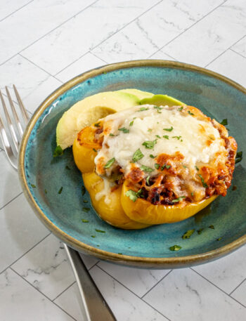 A chorizo-stuffed pepper with mozzarella cheese topping and sliced avocado on the side.