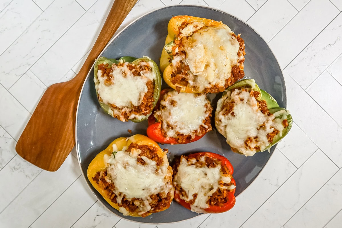 Peppers stuffed with chorizo and rice and topped with cheese, on a serving platter with a spatula alongside.