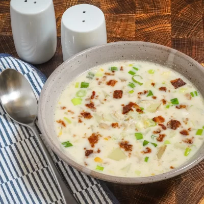 Creamy soup with green onions and crispy bacon bits in a beige bowl.