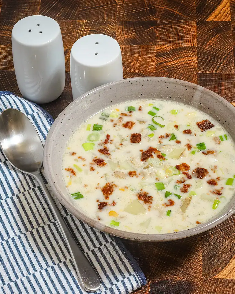Creamy soup with green onions and crispy bacon bits in a beige bowl.