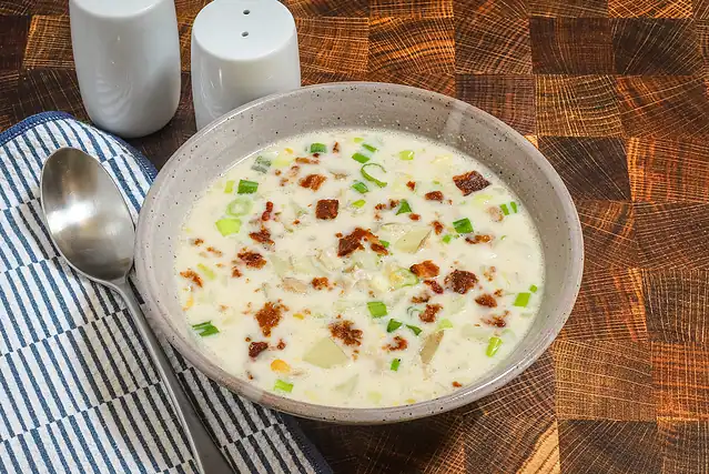 A bowl of clam and corn chowder with potatoes, green onions, and a bacon garnish.