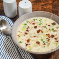 A bowl of clam and corn chowder with potatoes, green onions, and a bacon garnish.